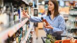 Woman,Making,A,Purchasing,Decision,,Holding,A,Bottle,And,Reaching